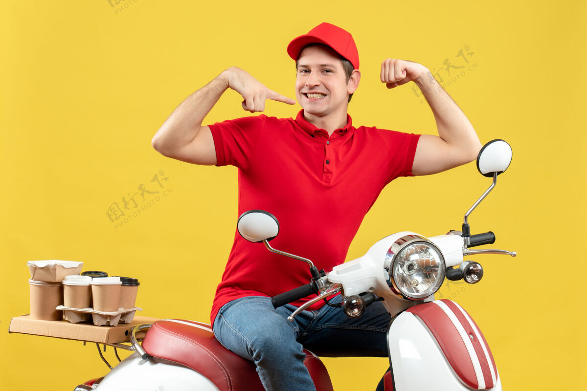 人俯视图：身穿红色上衣 头戴帽子的雄心勃勃的年轻人坐在踏板车上 在黄色背景上展示他的肌肉运动摩托车背景
