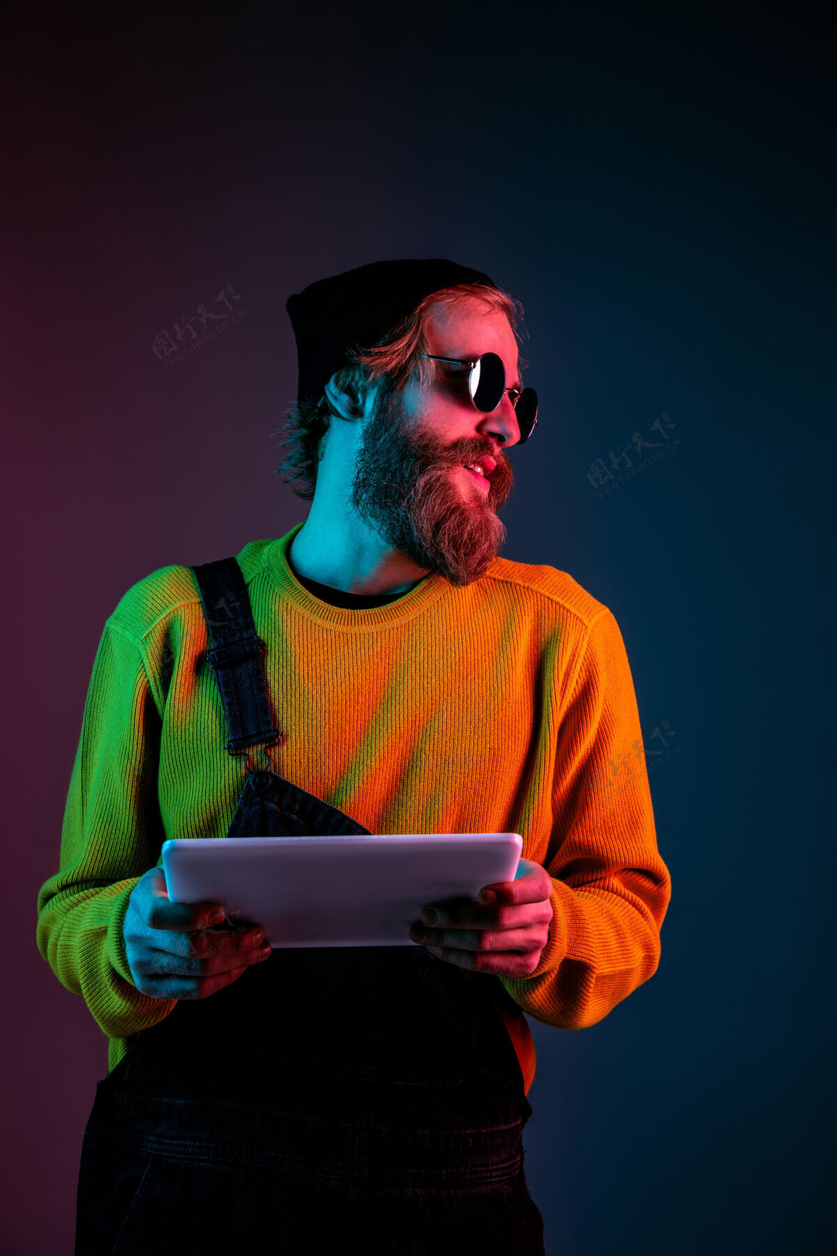 年轻使用平板电脑 看起来很快乐霓虹灯下渐变工作室背景上的白种人肖像时髦风格的漂亮男模人类情感的概念 面部表情 销售 广告衬衫公司一半