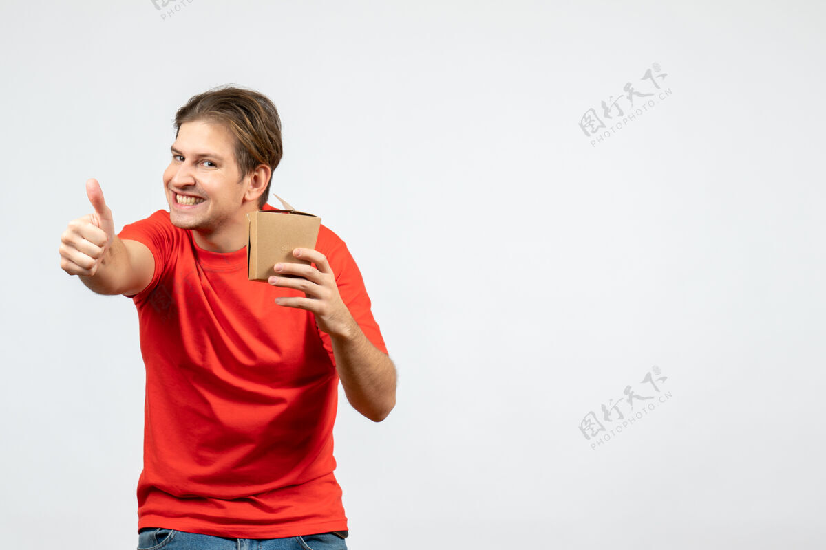男性正面图是一个微笑的年轻人 穿着红色上衣 手里拿着一个小盒子 在白色背景上做着“ok”的手势手势好手持