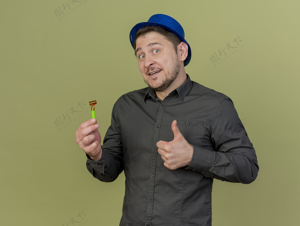 举行微笑着的年轻人穿着黑色衬衫 戴着蓝色帽子 举着吹风机在橄榄绿上孤立地竖起大拇指拇指蓝色家伙