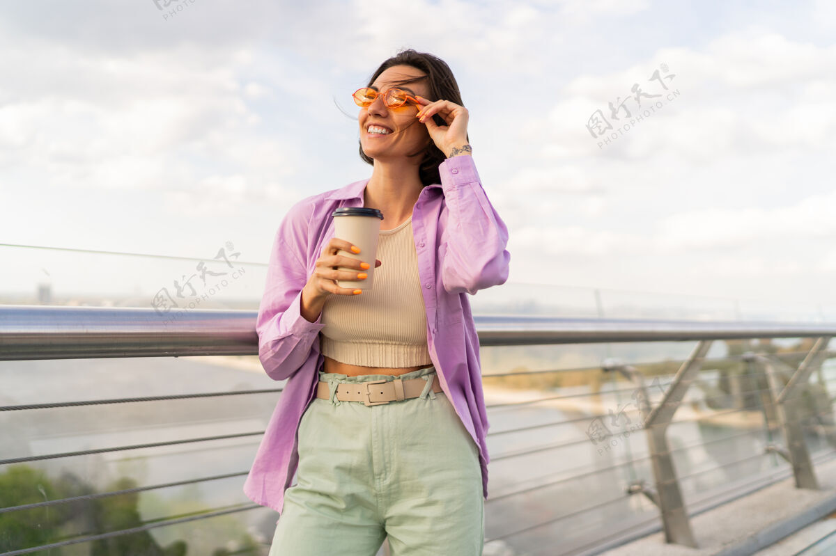 阳光一个可爱的短发女人 在风和日丽的夏日走在摩登的桥上女性咖啡快乐