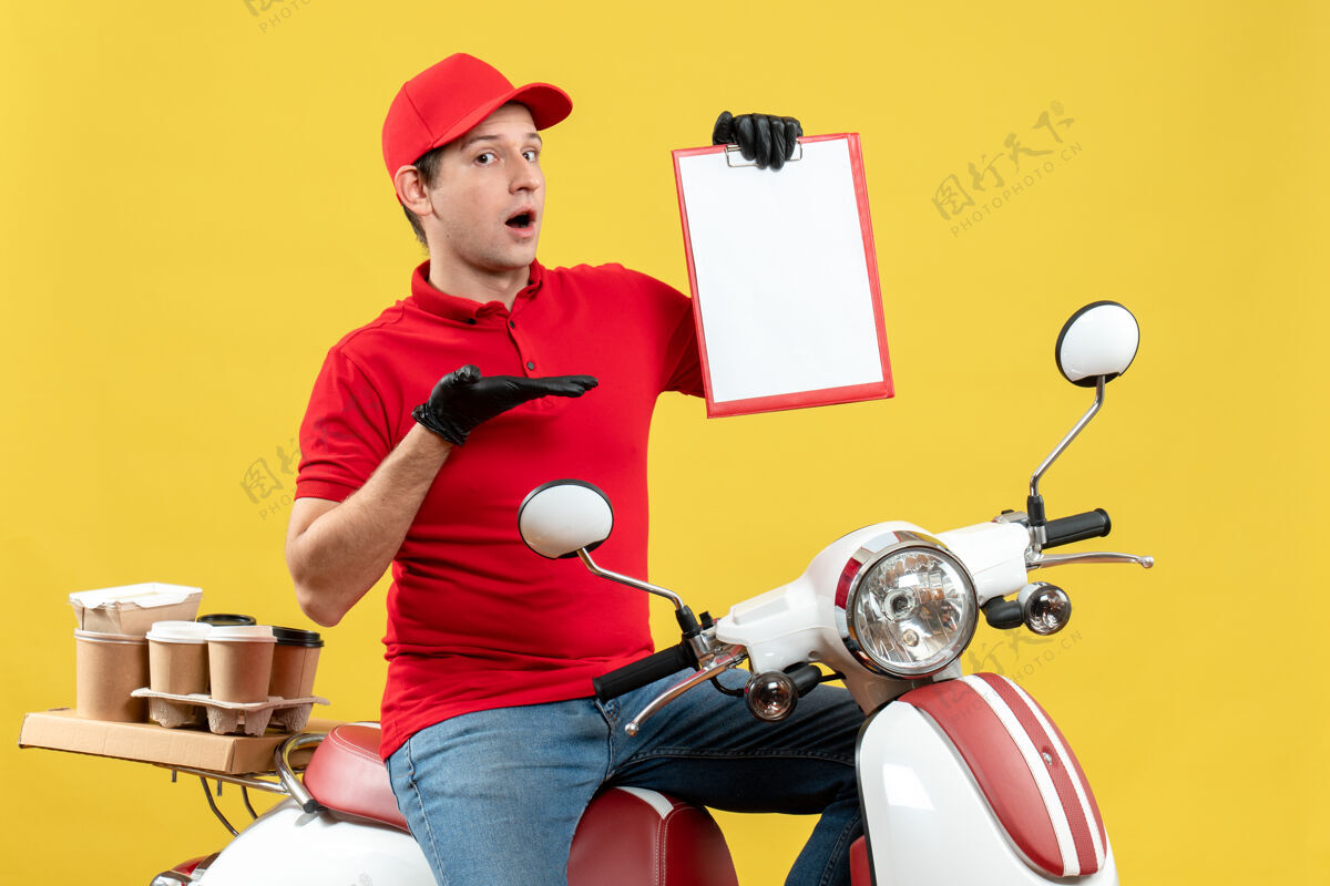 交付前视图好奇的信使男子穿着红色上衣 戴着帽子手套 戴着医用口罩 坐在滑板车上拿着文件传递订单医疗举行车辆