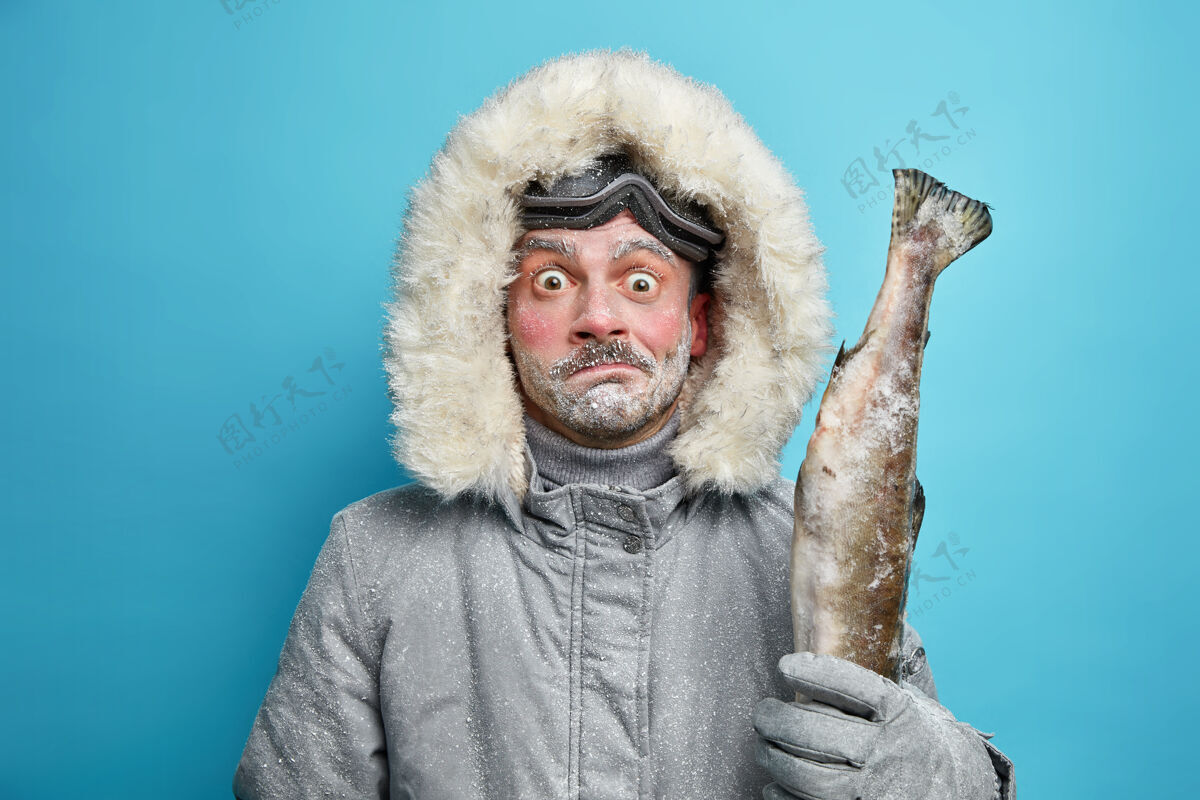 拼图在严寒的天气里 一个被冻住的男人穿着灰色的冬衣 戴着手套 抱着鱼 戴着滑雪眼镜 在户外呆了很长时间断绝男人爱好