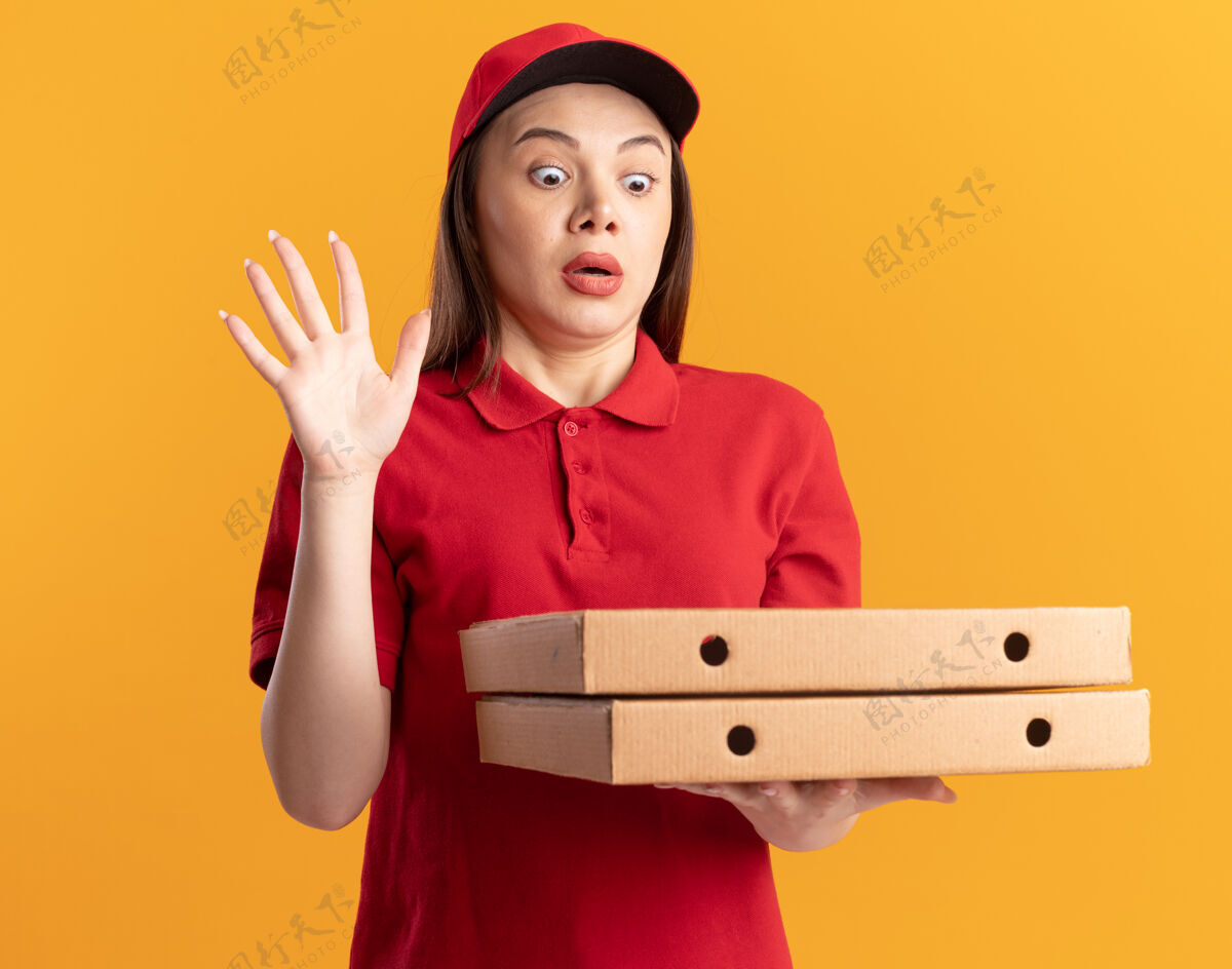 盒子穿着制服的焦急漂亮的女送货员站在那里 举起手 手里拿着橘色的披萨盒站披萨提高