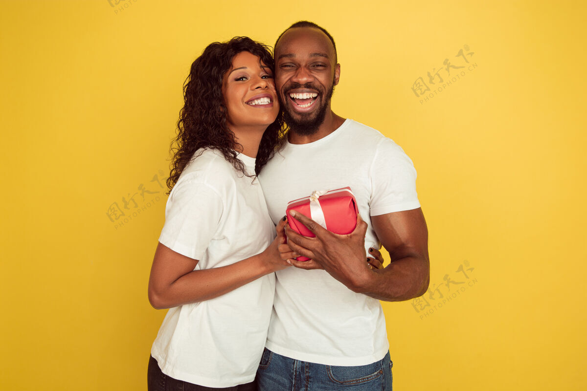 女孩给人惊喜情人节庆祝 快乐的非洲裔美国夫妇隔离在黄色的工作室背景人类情感的概念 面部表情 爱情 关系 浪漫的节日情感心微笑