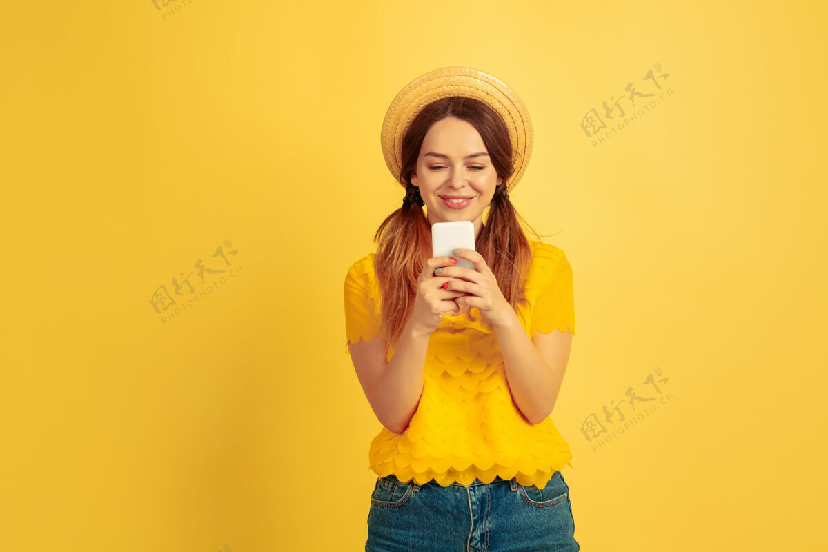 一半快乐使用智能手机黄色工作室背景上的白种女人肖像戴帽子的漂亮女模特人类情感的概念 面部表情 销售 广告夏日 旅游 度假主管情感女性