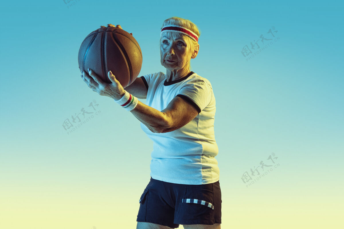 玩运动装的高级女性在渐变背景下打篮球 霓虹灯身材匀称的女性模特保持活跃运动 活动 运动 健康 自信的概念复制空间运动姿势运动