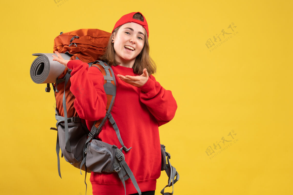 男人正面图：戴着红帽子的快乐女旅行者指着她的背包快乐指着帽子
