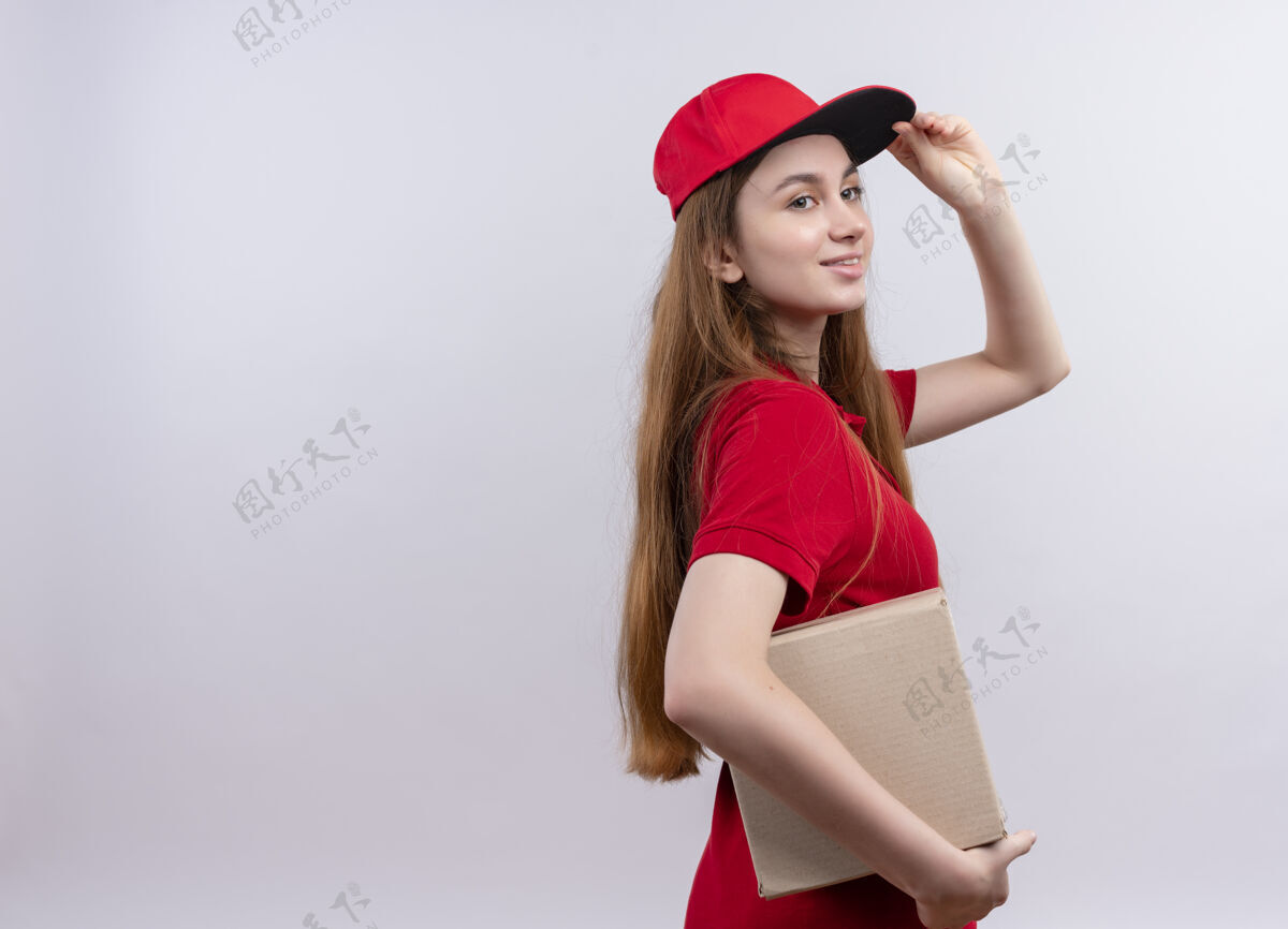 复制微笑着的年轻送货女孩 穿着红色制服 手放在帽子上 站在侧视图中 在一片空白处 留有复印空间手制服年轻