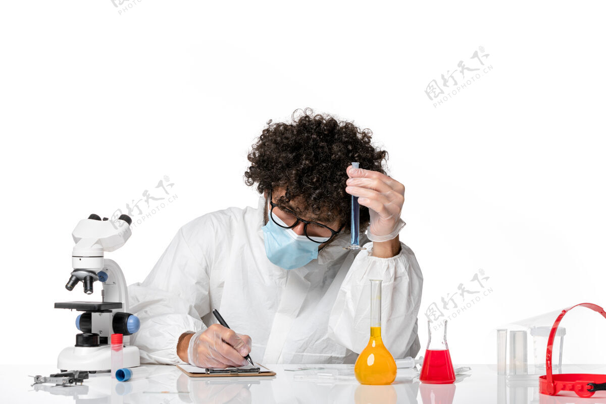 烧瓶正面图：男医生穿着防护服 戴着口罩 拿着装有蓝色溶液的烧瓶 背景是白色的流行性冠状病毒-流行性病毒防护视图流行病