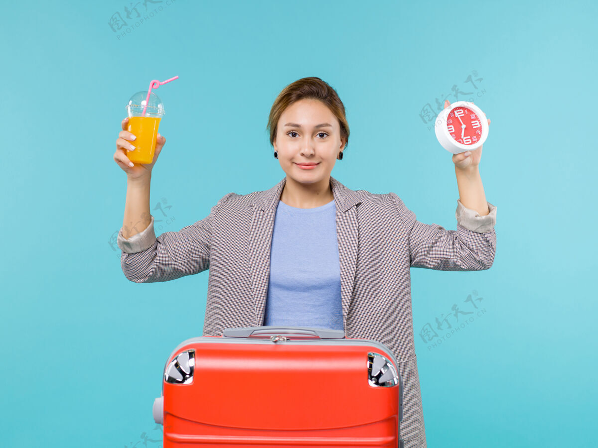 旅行正面图：度假中的女性手持新鲜果汁和蓝色背景上的时钟远航度假之旅海上之旅女人人果汁