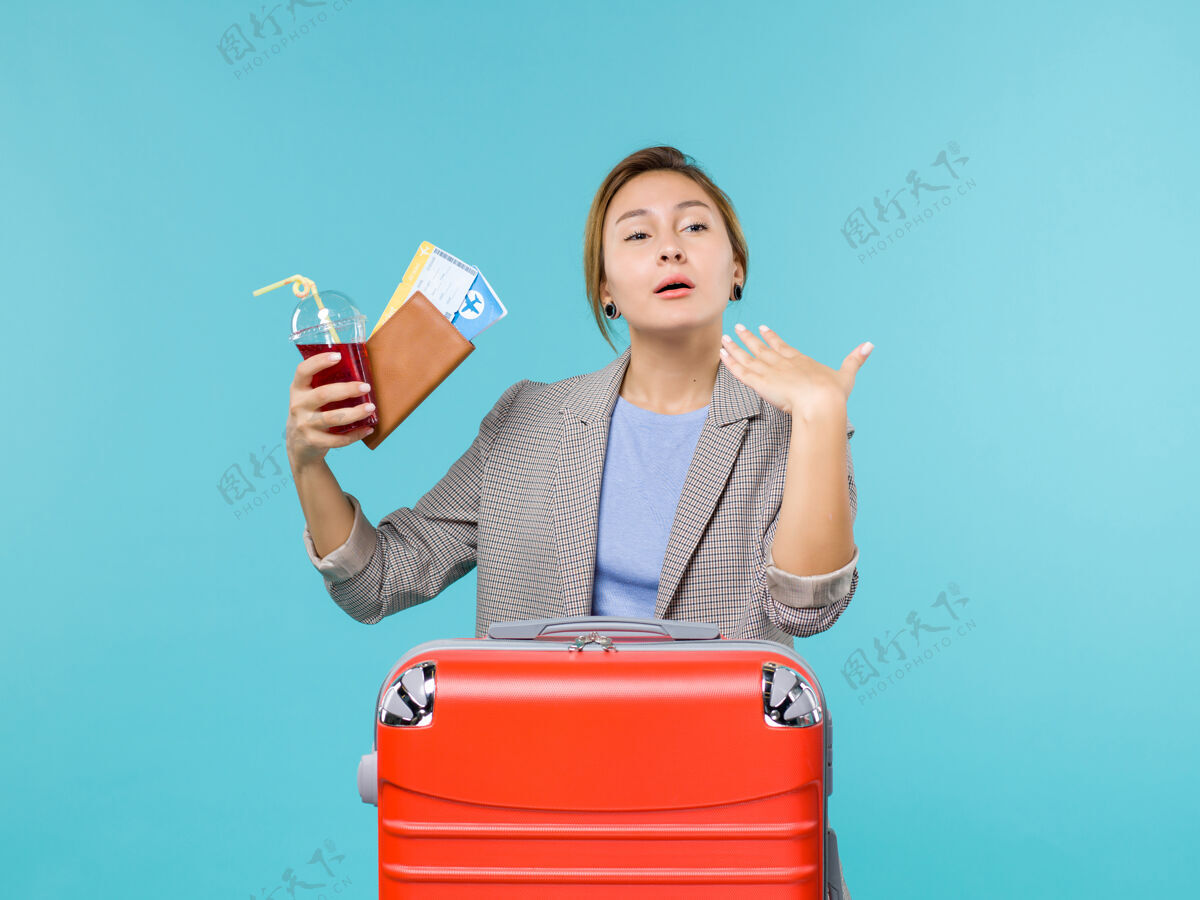 人正面图：度假中的女性拿着果汁和机票在蓝色的办公桌上旅行 飞机旅行 海上旅行旅行旅行前面