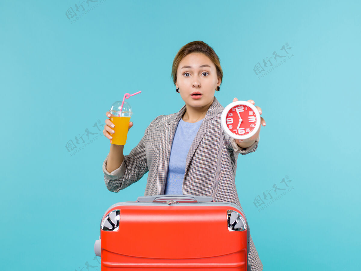 航行前景：度假中的女性手持新鲜果汁和时钟在蓝色背景上远航远航远航度假风景蓝色果汁