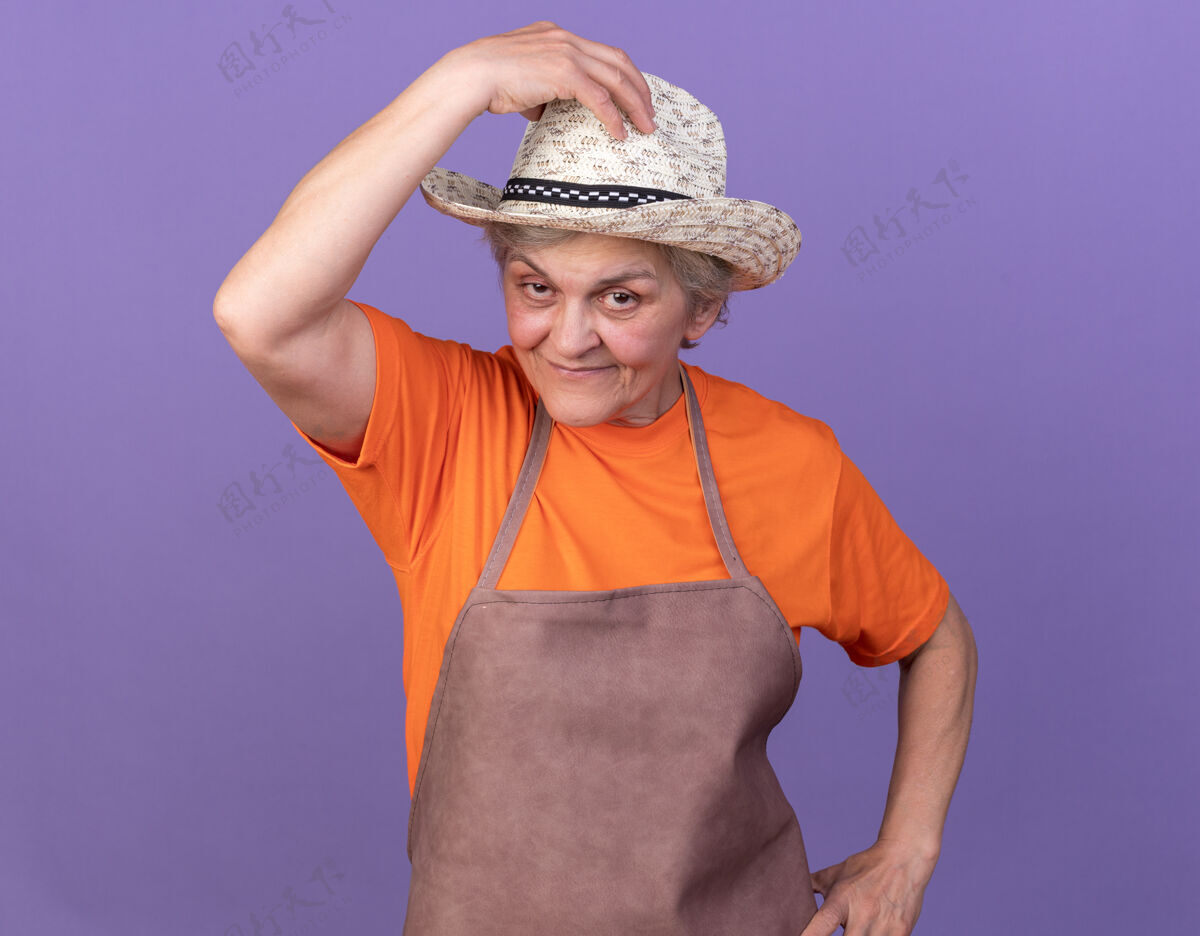 女高兴的上了年纪的女园丁戴着园艺帽把手放在紫色的帽子上老人花园帽子