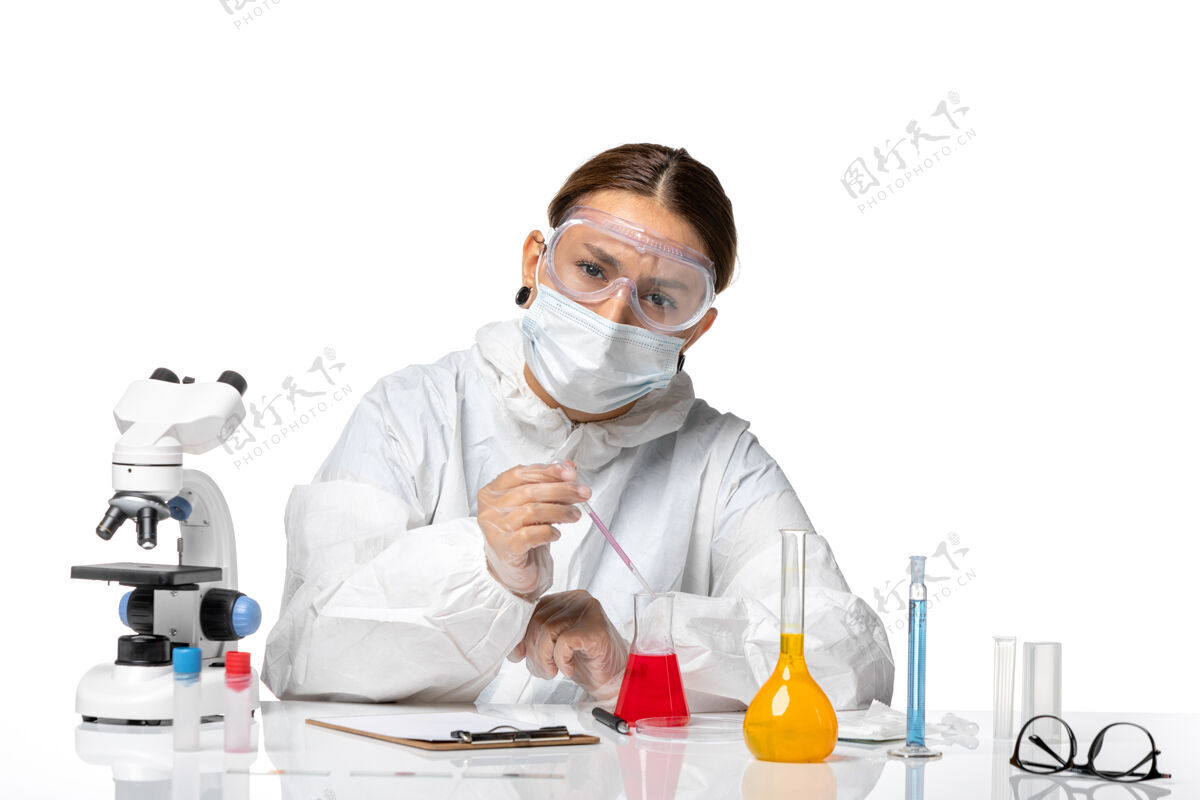 专业前视图穿着防护服 戴着口罩的女医生正在用白色背景的冠状病毒大流行病毒的解决方案工作实验室防护医院