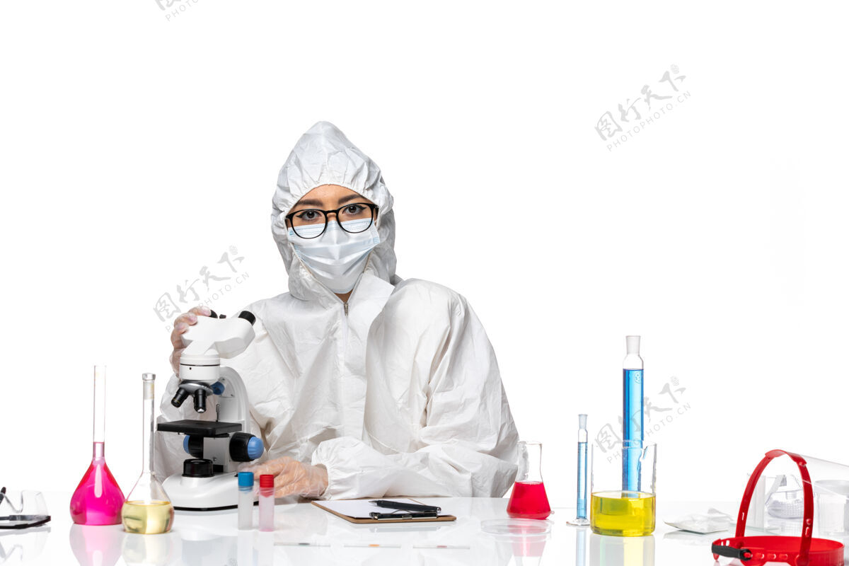面具前视图穿着特殊防护服的女化学家在白色背景的化学病毒实验室里用显微镜工作化学专业套装