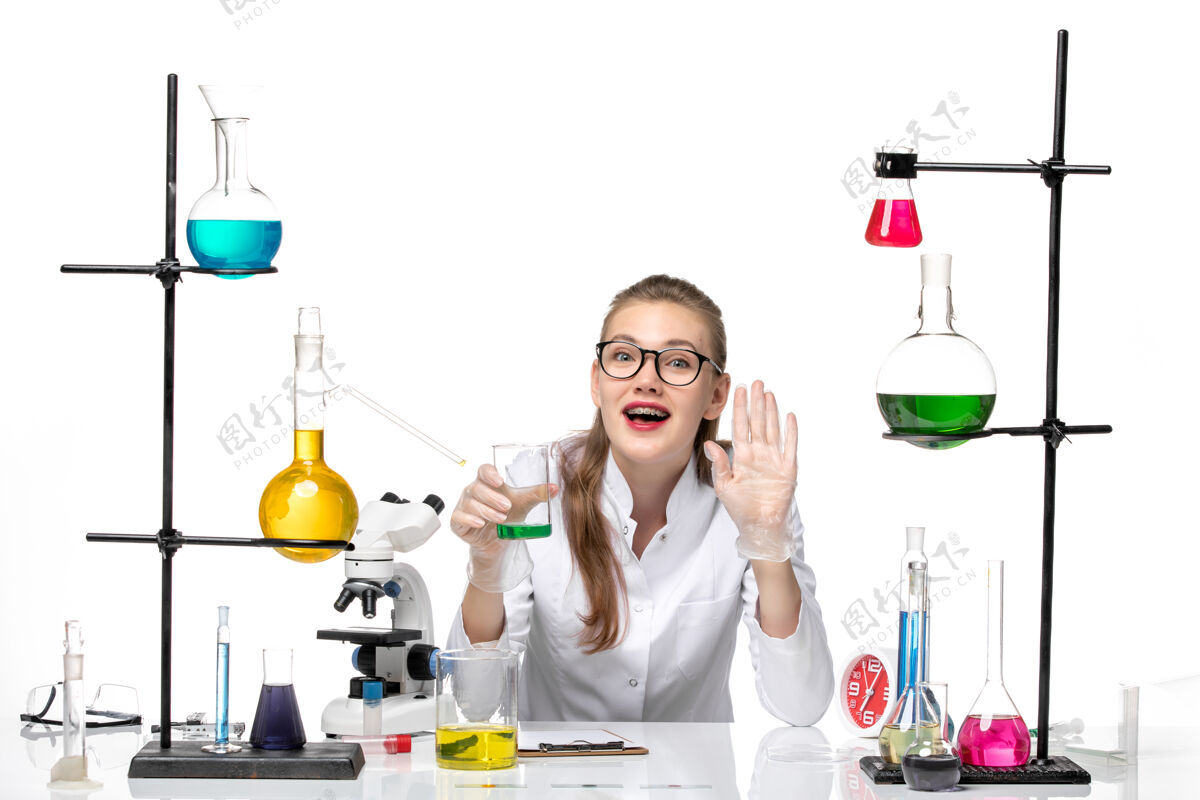 实验前视图穿着医疗服的女化学家拿着浅白色背景上有溶液的烧瓶化学大流行性健康病毒白色实验室容器