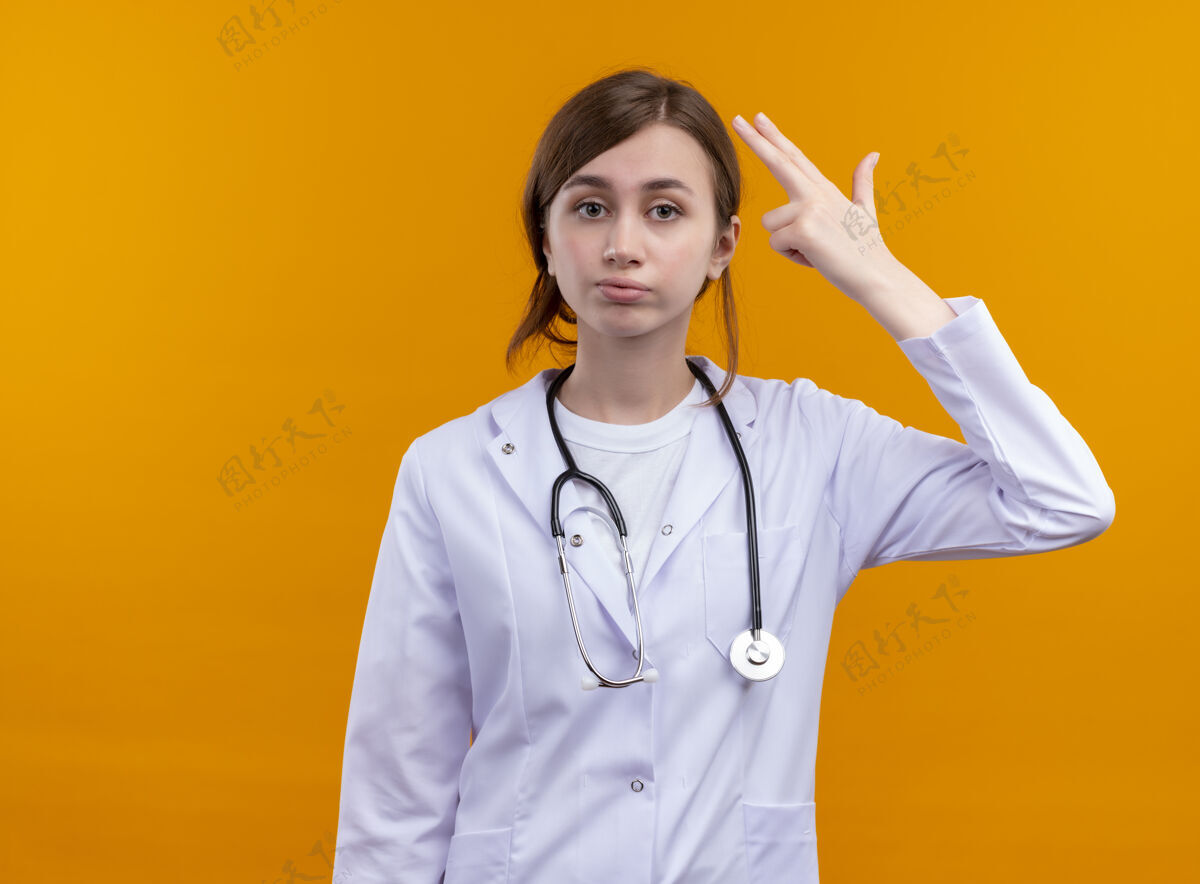 女性厌倦了年轻的女医生穿着医用长袍和听诊器在孤立的橙色空间里做自杀的手势橙色医疗太空