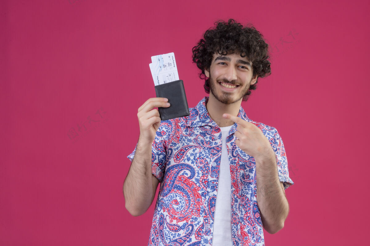 年轻快乐的年轻帅气的卷发旅行者 在有复印空间的粉色空间里 展示机票和钱包 并指着它们指向旅行者粉色
