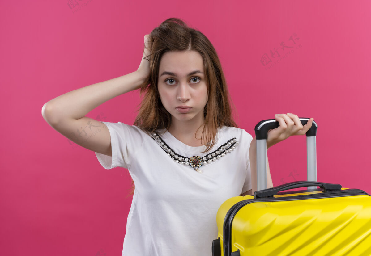 自信自信的年轻旅行家女孩拿着手提箱 把手放在孤立的粉红色空间头上粉色女孩手提箱
