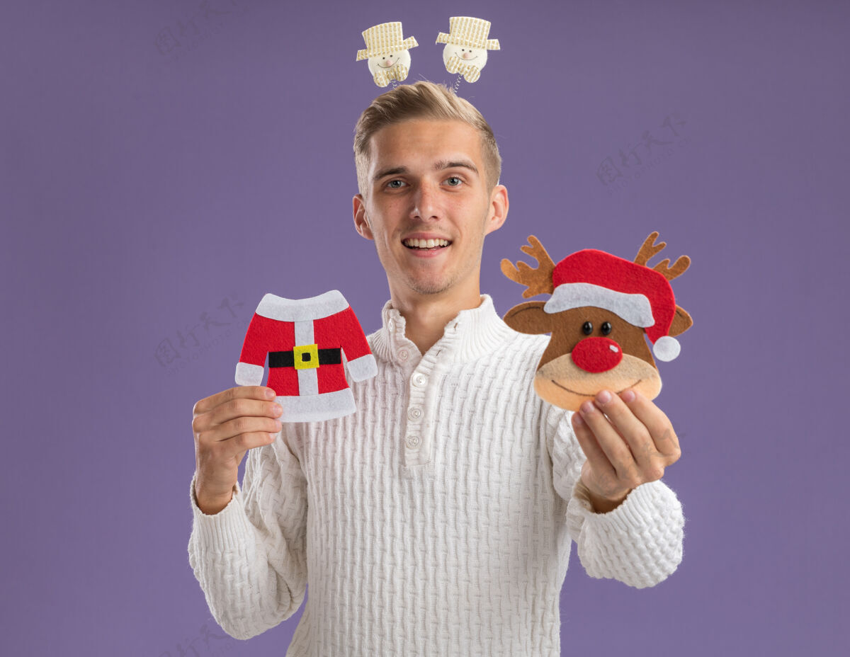抱着印象深刻的年轻帅哥戴着雪人头带 拿着圣诞纸饰品 对着镜头望着隔离在紫色背景上的镜头紫色雪人圣诞快乐