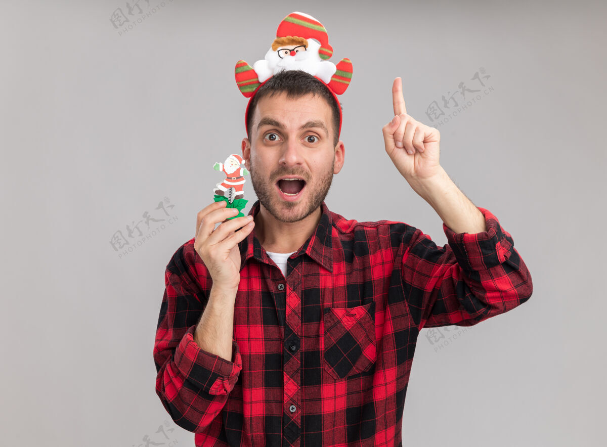 圣诞老人令人印象深刻的年轻白种人戴着圣诞老人的头带拿着雪人圣诞玩具看着相机指着孤立的白色背景雪人指向复制