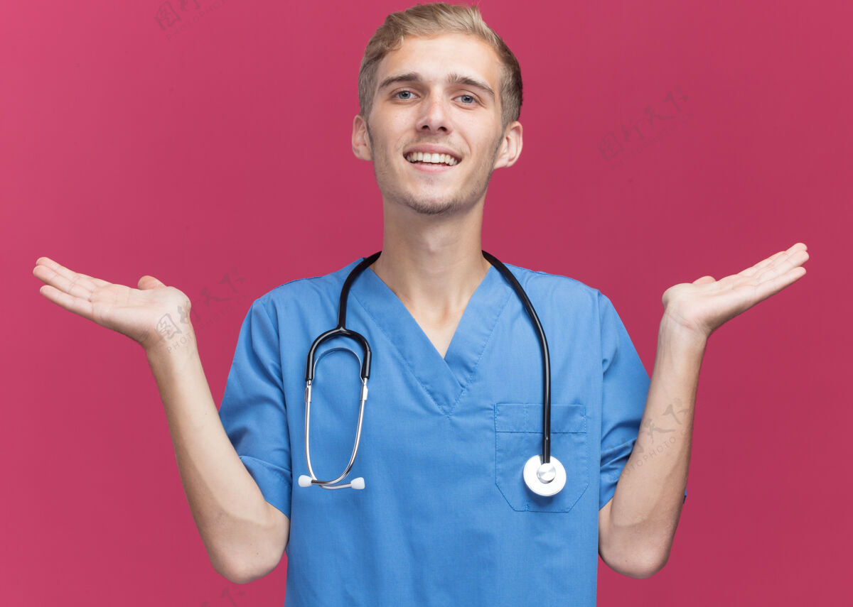 公民微笑着的年轻男医生穿着医生制服 听诊器摊开双手隔离在粉红色的墙上衣服姿势人
