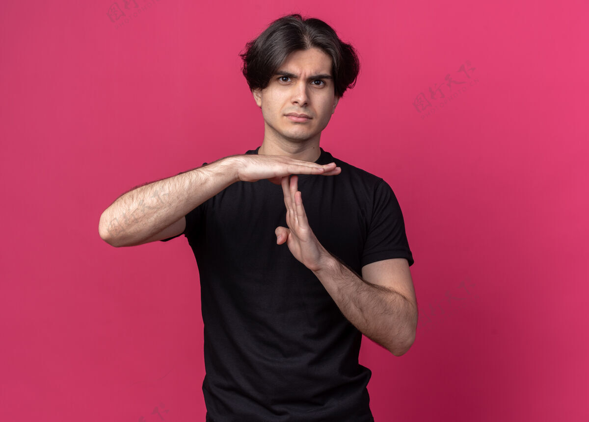 严格穿着黑色t恤的年轻帅哥 在粉红色的墙上显示出一个孤立的手势感觉脸衣服