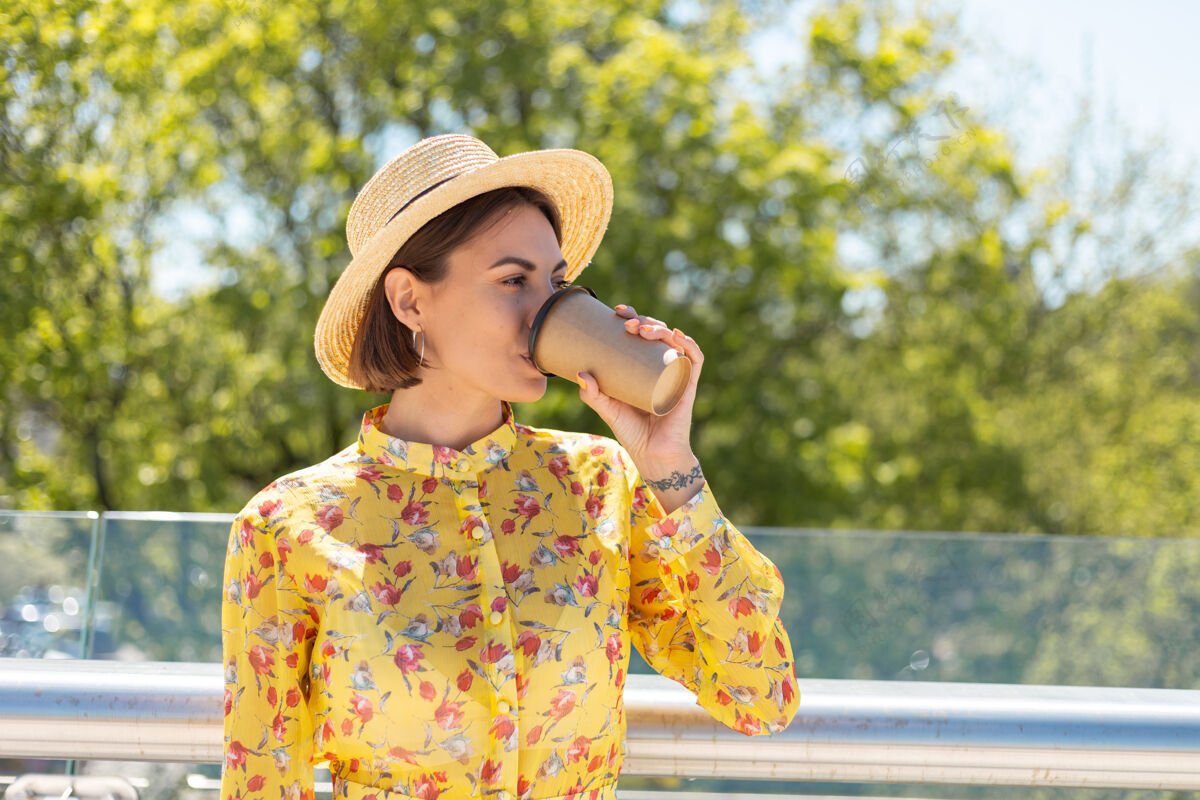 休闲穿着黄色夏装 戴着帽子 喝着咖啡 享受阳光的女人的户外肖像自由人户外