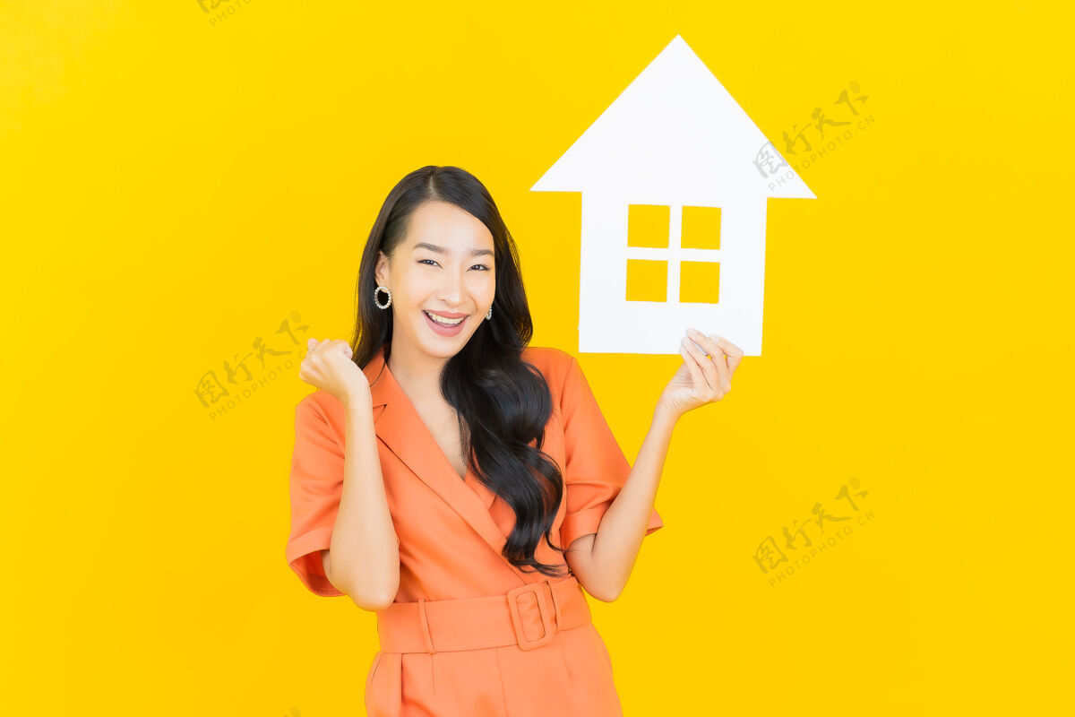 所有权肖像美丽的亚洲年轻女子微笑着用黄色的家庭标志纸板房子模型购买
