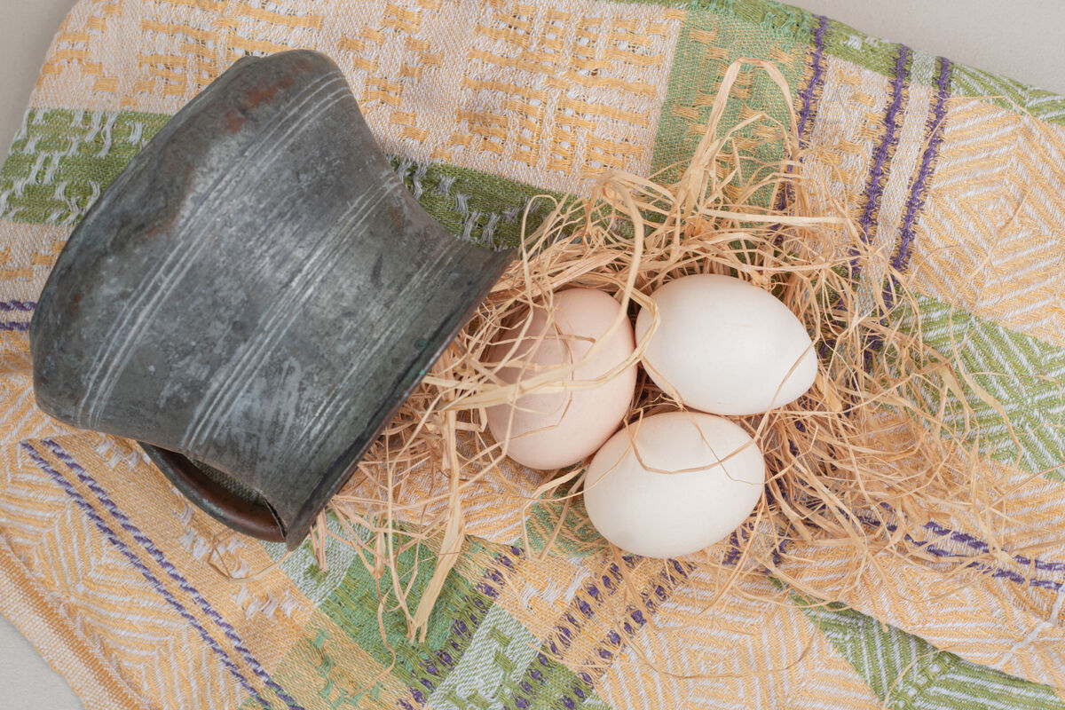 古代新鲜的鸡蛋和干草放在桌布上的古代杯子里食物生的杯子