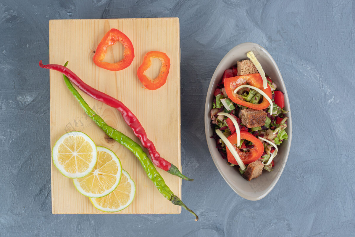 萝卜在大理石桌上的木板旁边放着蔬菜沙拉 上面放着智利胡椒和柠檬片和甜椒美味美味美味