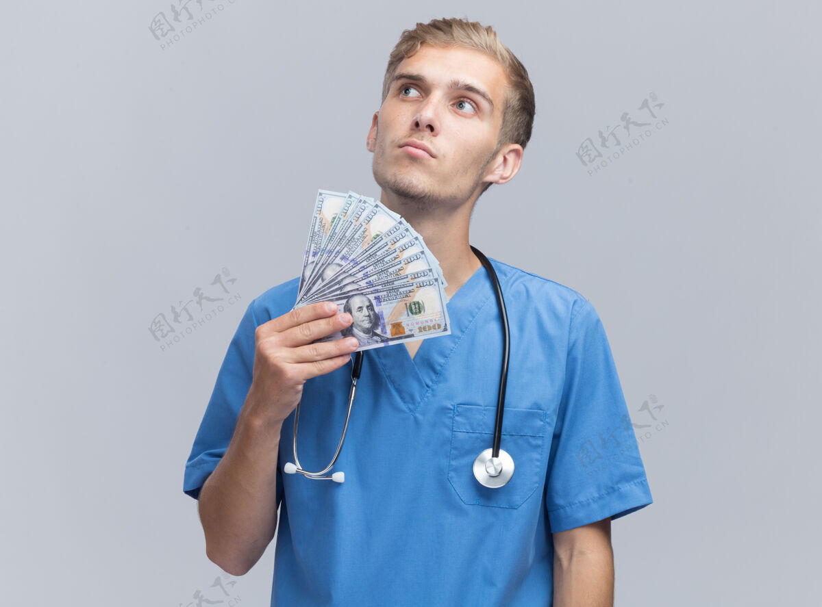 表情想着看着身边年轻的男医生穿着医生制服拿着听诊器把钱隔离在白墙上医生壁板人