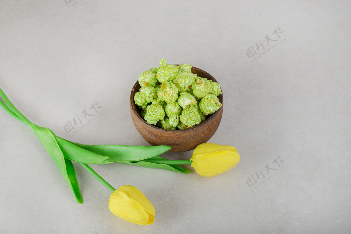 花黄色的郁金香和一碗爆米花糖放在大理石桌上垃圾食品芳香自然