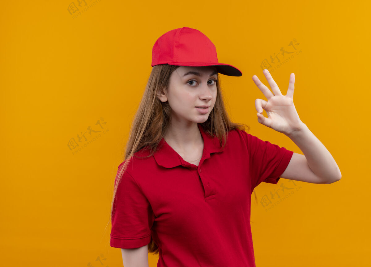 自信穿着红色制服的自信的年轻送货女孩在孤立的橙色空间和复印空间上做ok标志传递空格女孩
