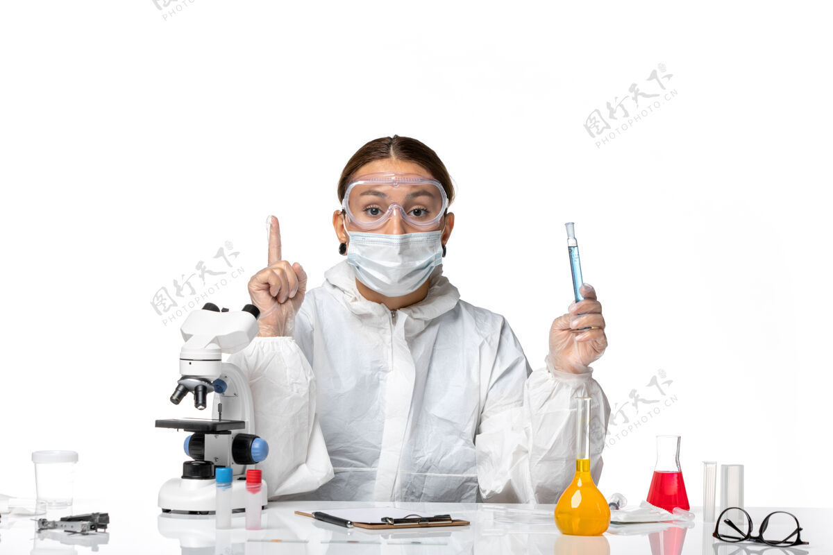 白色前视图：女医生穿着防护服 戴着口罩 拿着装有白色背景病毒冠状病毒溶液的烧瓶外套实验室外套工作服