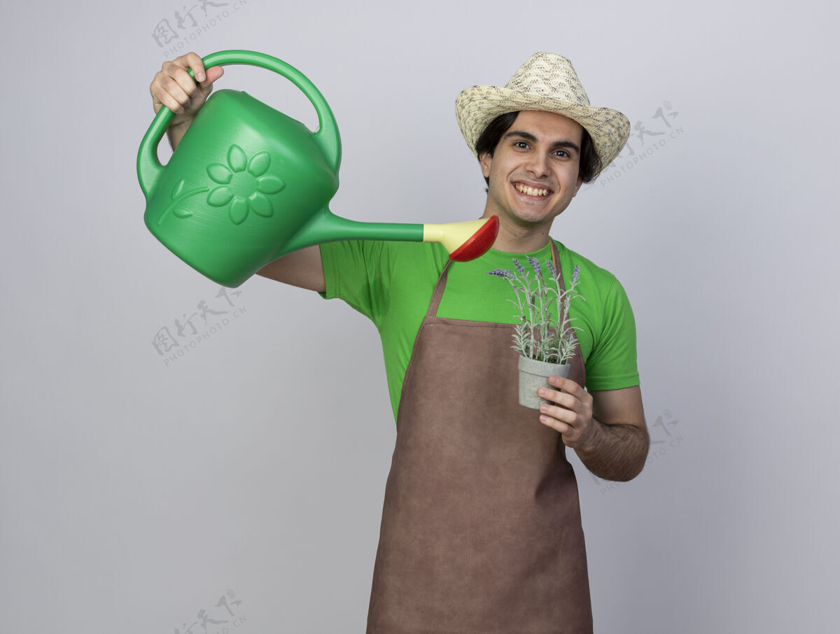 园艺微笑着的年轻男园丁穿着制服戴着园艺帽在花盆里用水壶浇花抱着帽子男人