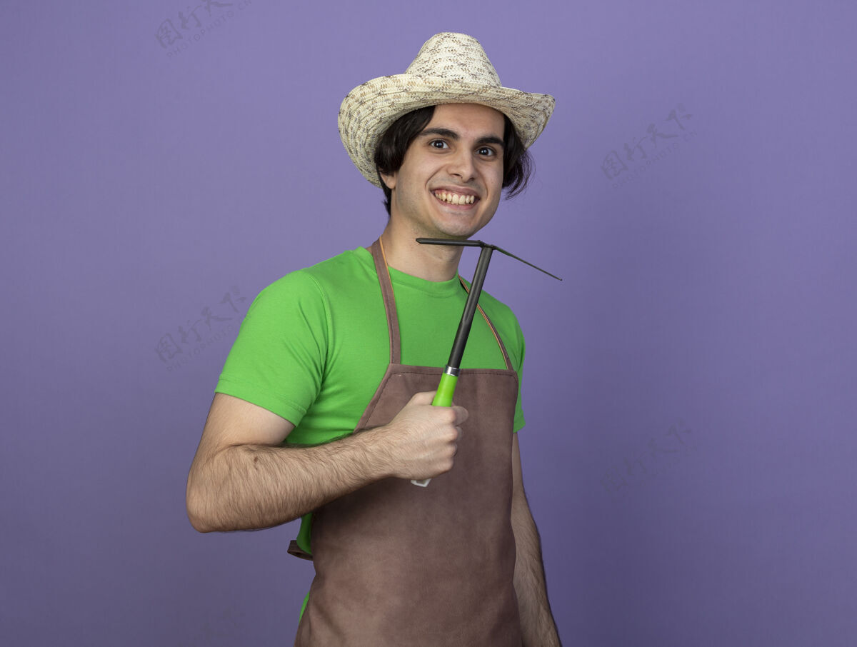男人微笑着的年轻男园丁穿着制服戴着园艺帽拿着锄头耙子年轻园艺紫色