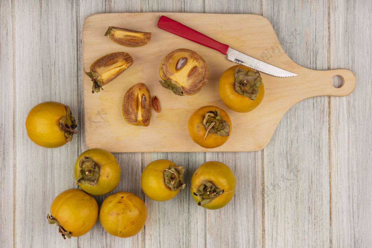 板黄色柿子水果的顶视图在一个木制的厨房板上 在灰色的木制桌子上放着一把刀灰色刀橘子