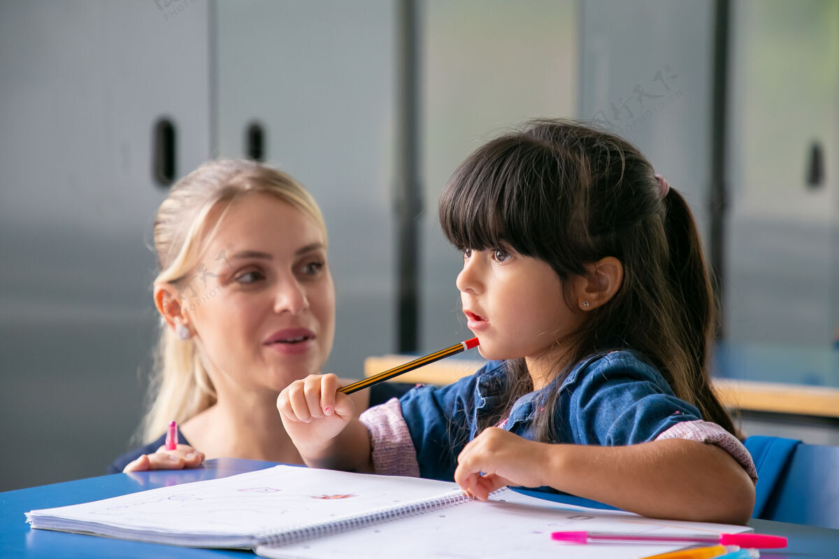 幼儿园开朗的年轻教师帮助小女生完成任务孩子笔记本学习
