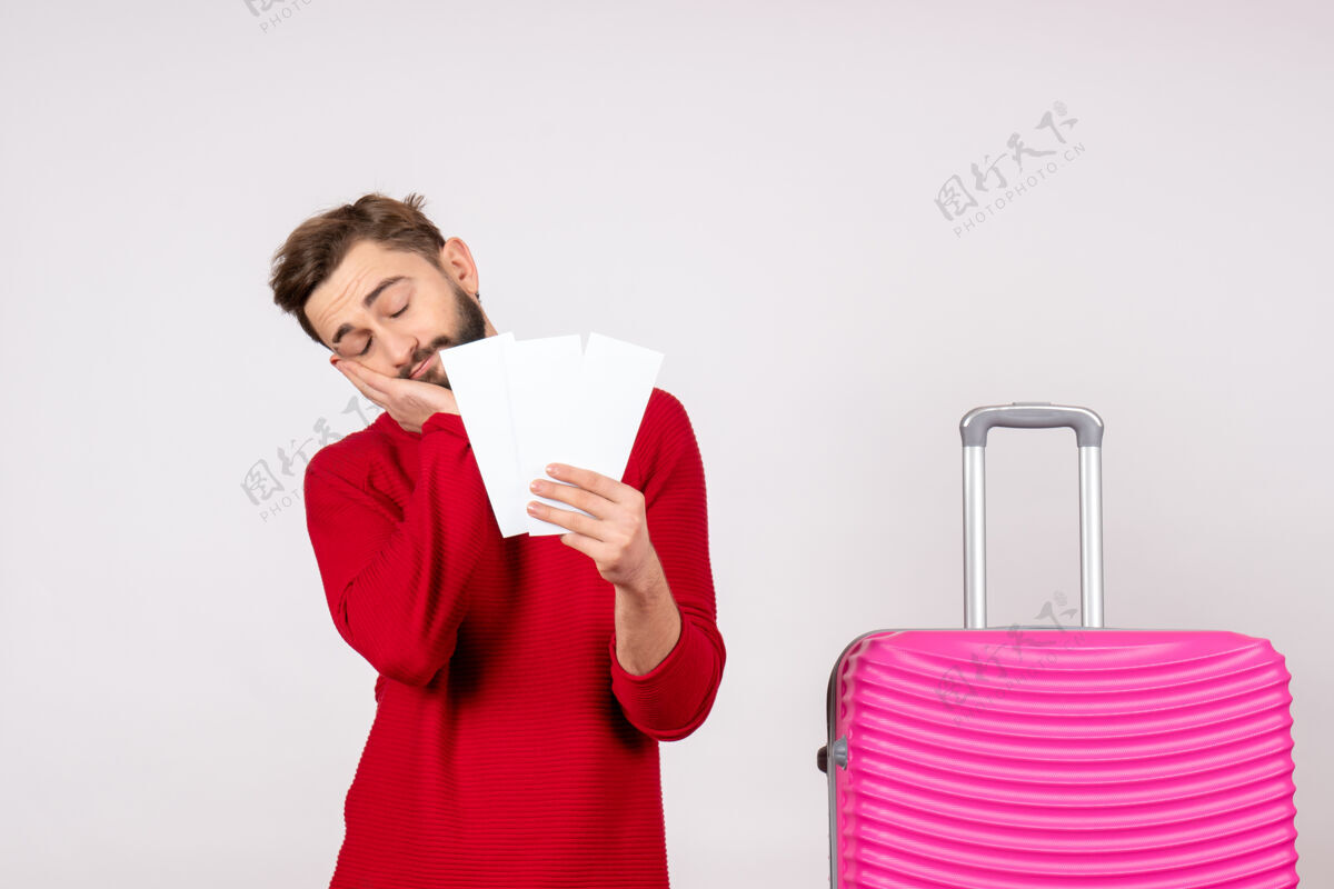 度假正面图：年轻男性 带着粉红色的包 拿着票 在白色的墙壁上感到疲惫 航行 飞行 彩色旅行 旅游度假照片 情感情感航班年轻男性