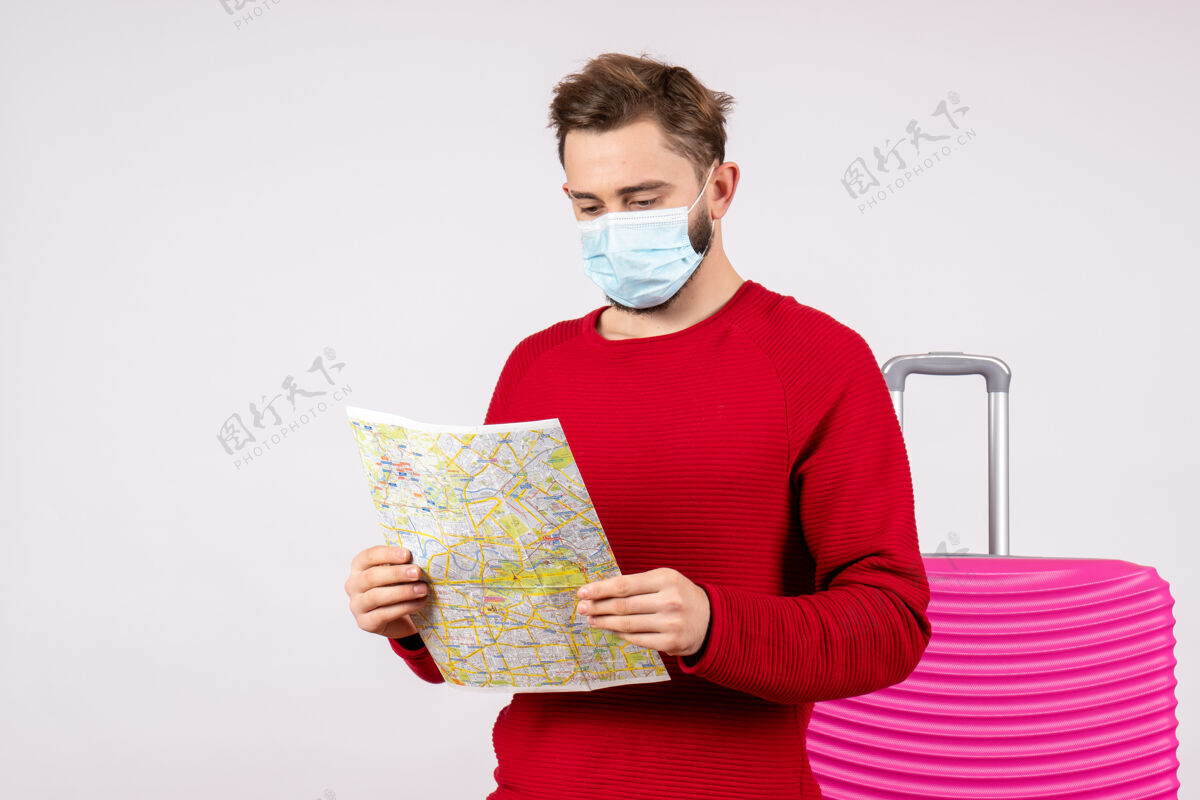 成人正面图：戴着面具的年轻男性手持白墙病毒航行图covid-飞行旅行度假色游客度假笔记本电脑