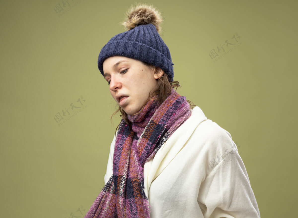 橄榄咳嗽的年轻生病的女孩穿着白色长袍 戴着冬天的帽子 围着橄榄绿的围巾围巾绿色帽子