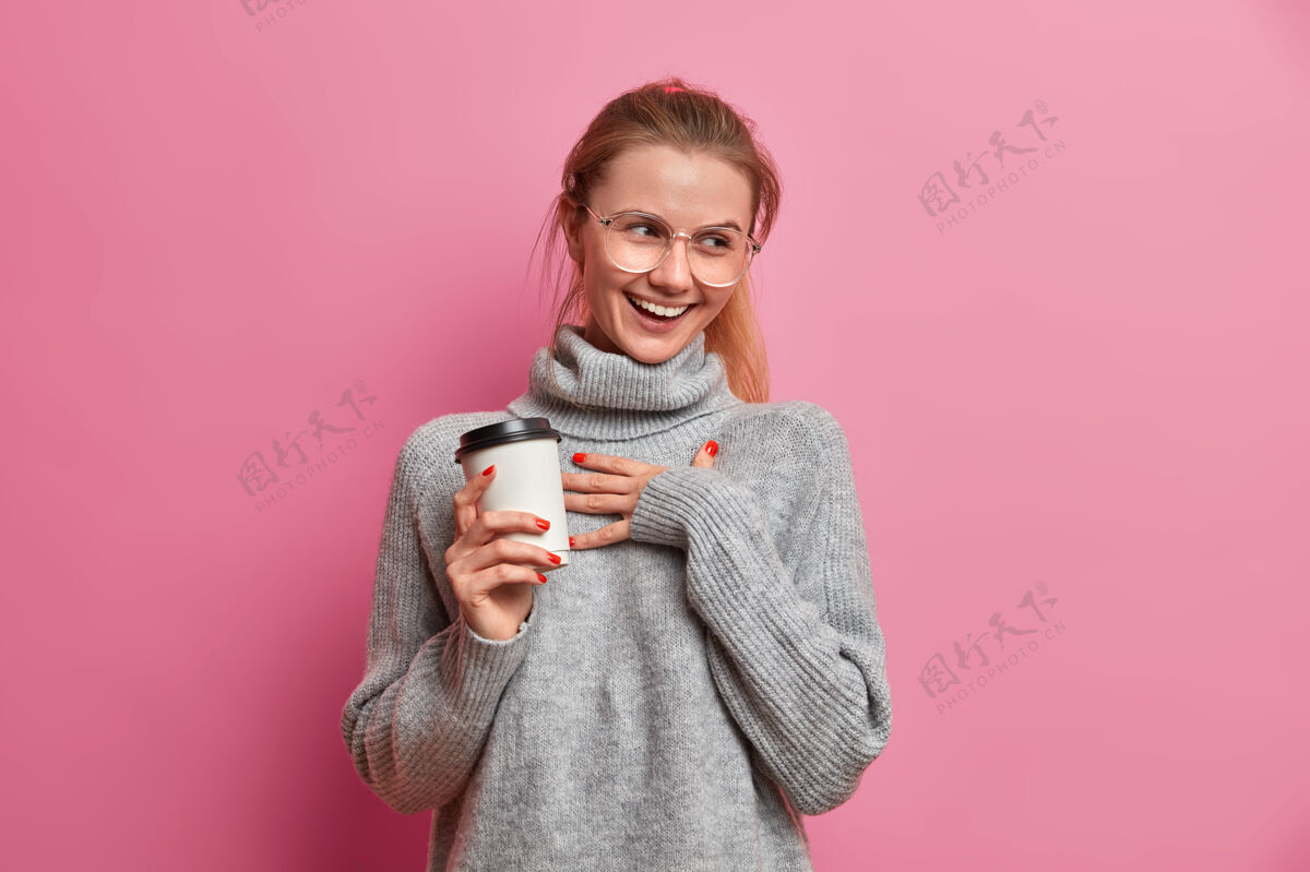 微笑摄影棚拍摄的欢快的欧洲女孩咯咯笑积极保持手放在胸前 并举行外卖咖啡高兴眼镜欢呼