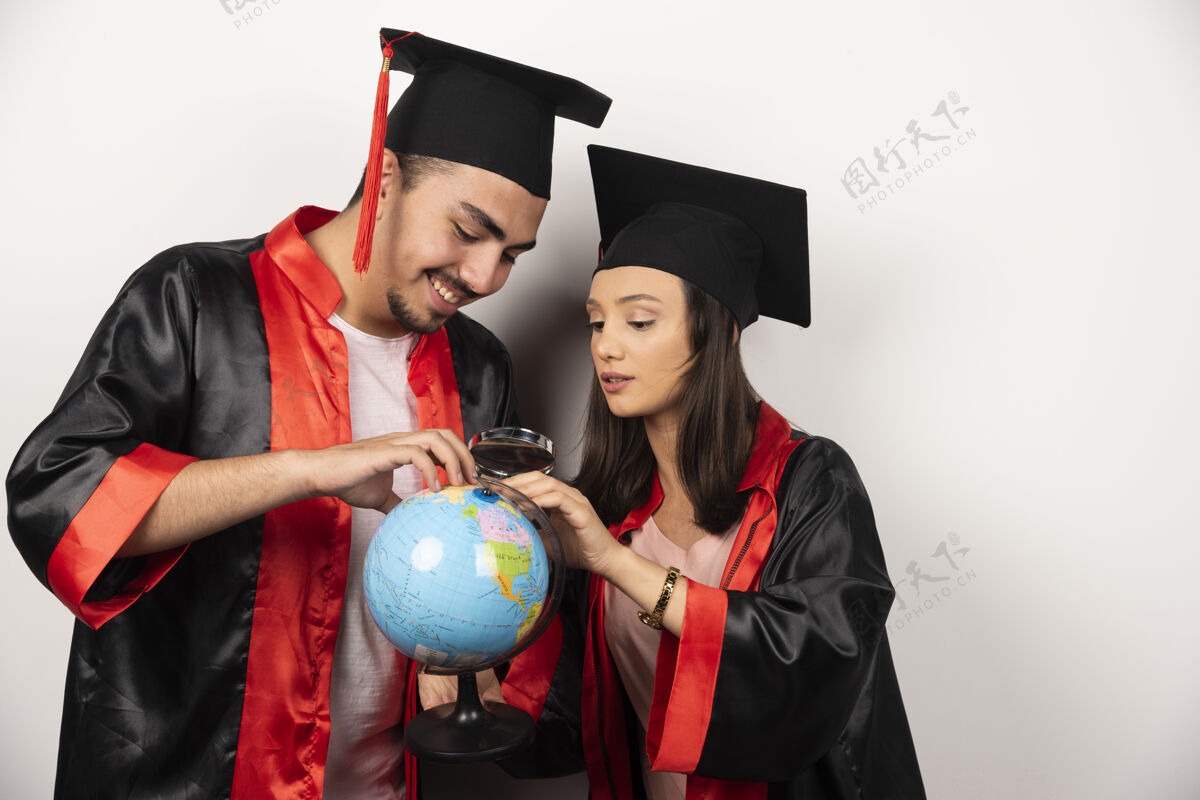 快乐一对穿着长袍的快乐学生看着白色的地球仪帽子年轻教育