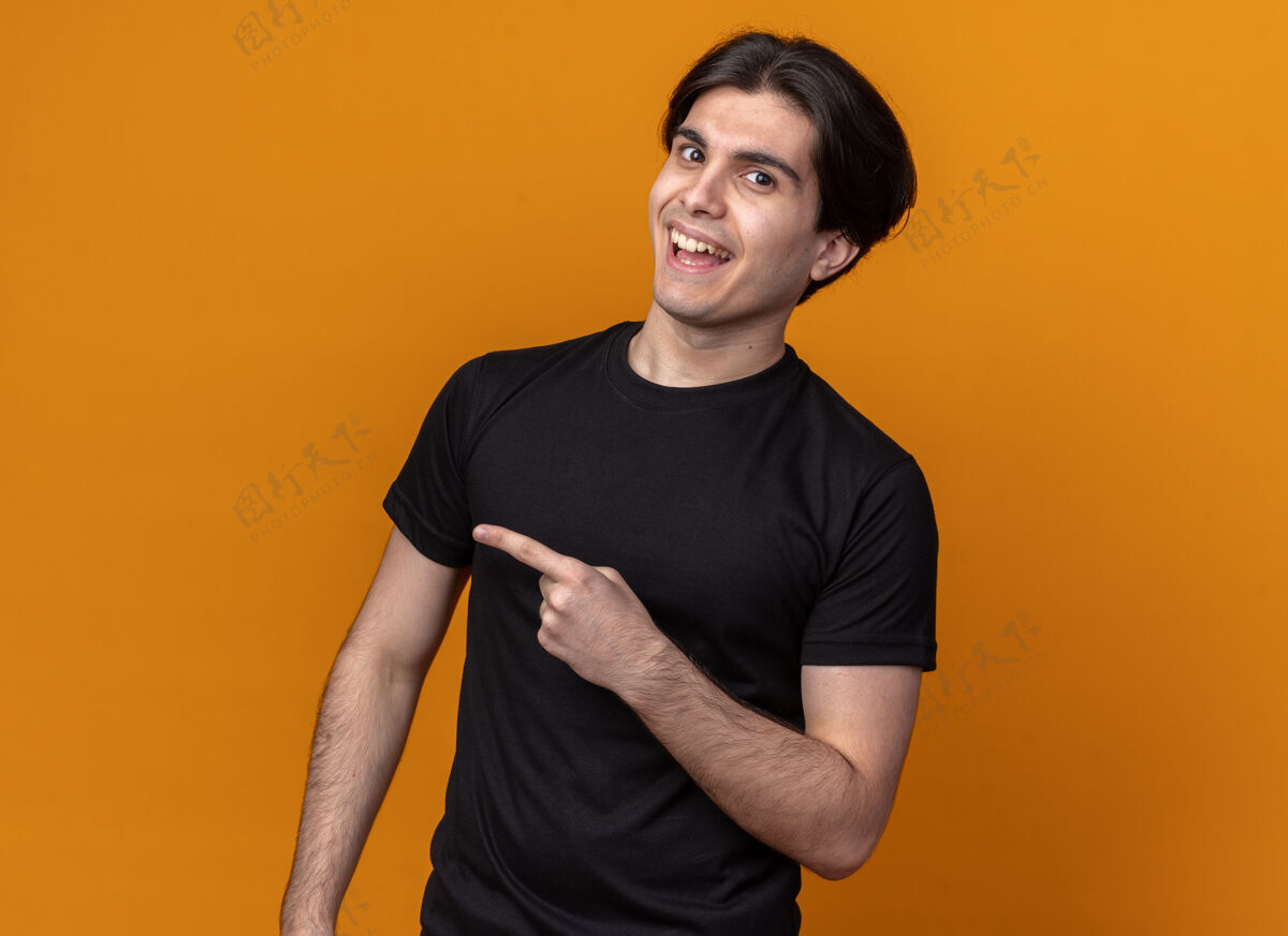 家伙快乐的年轻帅哥穿着黑色t恤点在一边 隔离在橙色的墙壁与复制空间点侧翼欢乐