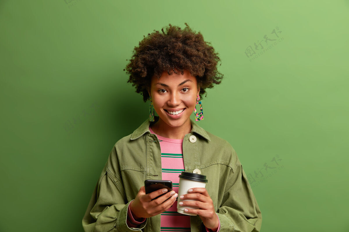 绿色摄影棚拍摄的黑皮肤年轻女子手持手机 带走咖啡非洲高兴年轻