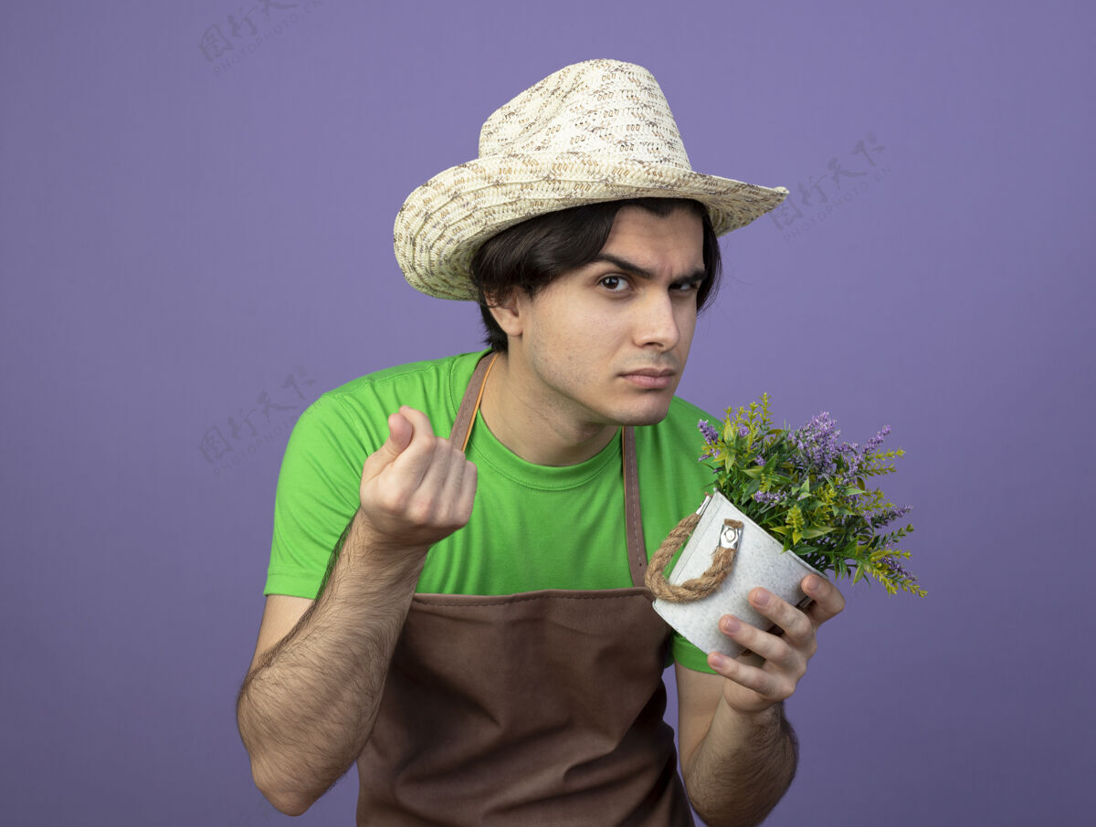 可疑可疑的年轻男园丁穿着制服 戴着园艺帽 在花盆里拿着花 表现出现金的姿态花花园展示