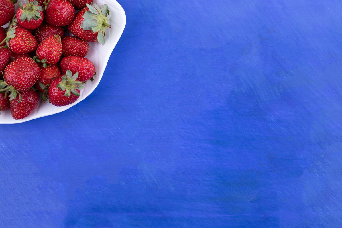 多在蓝色的表面上放满草莓的白色盘子刷新健康有机草莓
