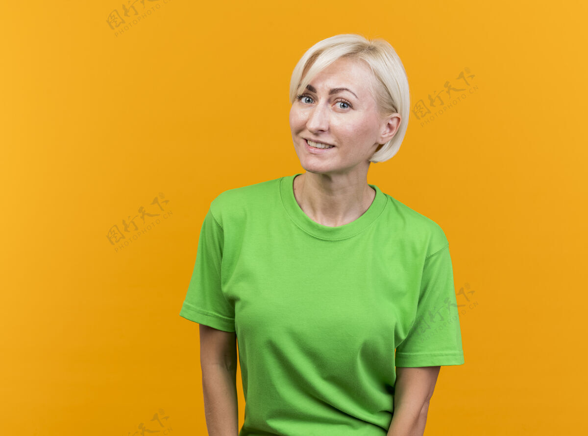女人微笑的中年金发斯拉夫妇女看着前面孤立的黄色墙壁与复制空间感觉姿势金发